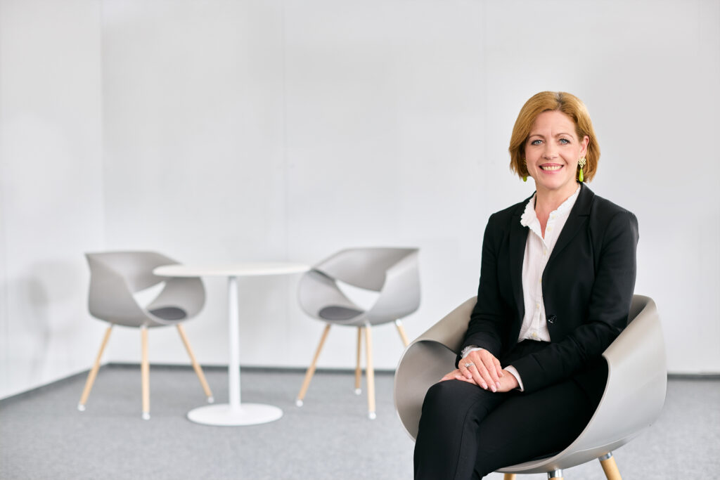 Sabine Schoon-Renné sitzt auf diesem Businessfoto auf einem Stuhl und schaut lächelnd in die Kamera.