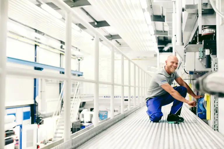 Industriefoto eines Mitarbeiters an einer Maschine. Er schaut in die Kamera.